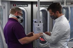Workers attach ultraviolet light-emitting fixtures on a stand pole inside a New York City Metro Transit Authority subway car. Workers attach ultraviolet light-emitting fixtures on a stand pole inside a New York City Metro Transit Authority subway car.