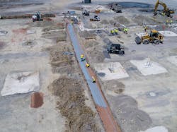 This aerial view shows electricians working in the field using a digital system to lay out conduit.