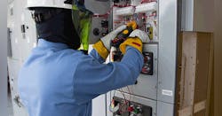 An electrical worker is geared up in arc flash workwear, which includes rubber insulated safety gloves, a hard hat, and face shield.