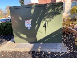 Green 34kV pad-mounted utility transformer sitting in the landscaped area next to a building Green 34kV pad-mounted utility transformer sitting in the landscaped area next to a building