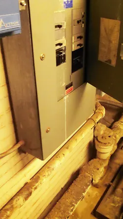 Plumbing pipes sitting below an electrical panelboard