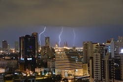 Three lightning bolts in nighttime sky with downtown buildings in foreground Three lightning bolts in nighttime sky with downtown buildings in foreground