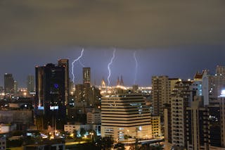 Three lightning bolts in nighttime sky with downtown buildings in foreground