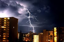 Lightning bolt in nighttime sky with large buildings in foreground