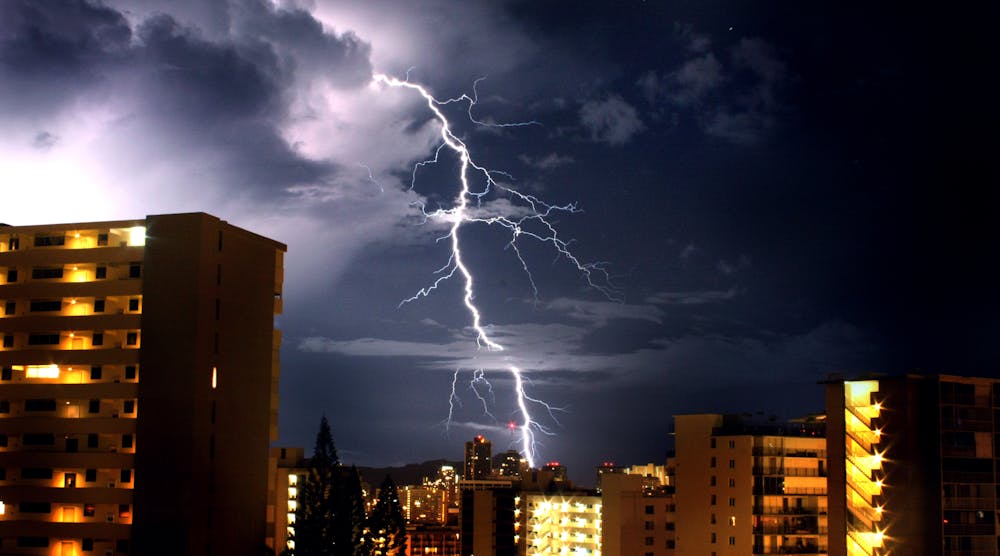 Lightning bolt in nighttime sky with large buildings in foreground