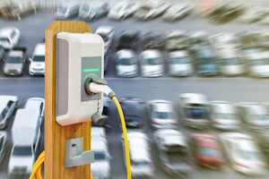 Electric vehicle charging unit with parking lot full of cars in background