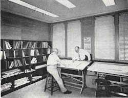 Two Men At A Drafting Table In A Group Office