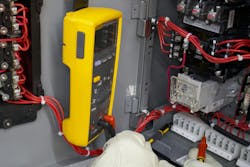 Photo 1. A good practice whether troubleshooting or maintenance testing is to clip the black test lead of a digital multimeter onto a common terminal and use the red test lead to “probe” at different points in the circuit to measure voltage as applicable. In this image, X2 is the common from the control power transformer and the red probe is testing for voltage at terminal 4 and can be easily moved to the next terminal when ready. The meter is supported by a magnetic strap attached to the panel door. Photo 1. A good practice whether troubleshooting or maintenance testing is to clip the black test lead of a digital multimeter onto a common terminal and use the red test lead to “probe” at different points in the circuit to measure voltage as applicable. In this image, X2 is the common from the control power transformer and the red probe is testing for voltage at terminal 4 and can be easily moved to the next terminal when ready. The meter is supported by a magnetic strap attached to the panel door.