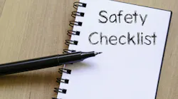 A notebook that says 'Safety Checklist' with a black pen (no cap) balancing on it. The notebook and pen are on a wooden background.