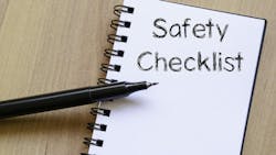 A notebook that says 'Safety Checklist' with a black pen (no cap) balancing on it. The notebook and pen are on a wooden background. A notebook that says 'Safety Checklist' with a black pen (no cap) balancing on it. The notebook and pen are on a wooden background.