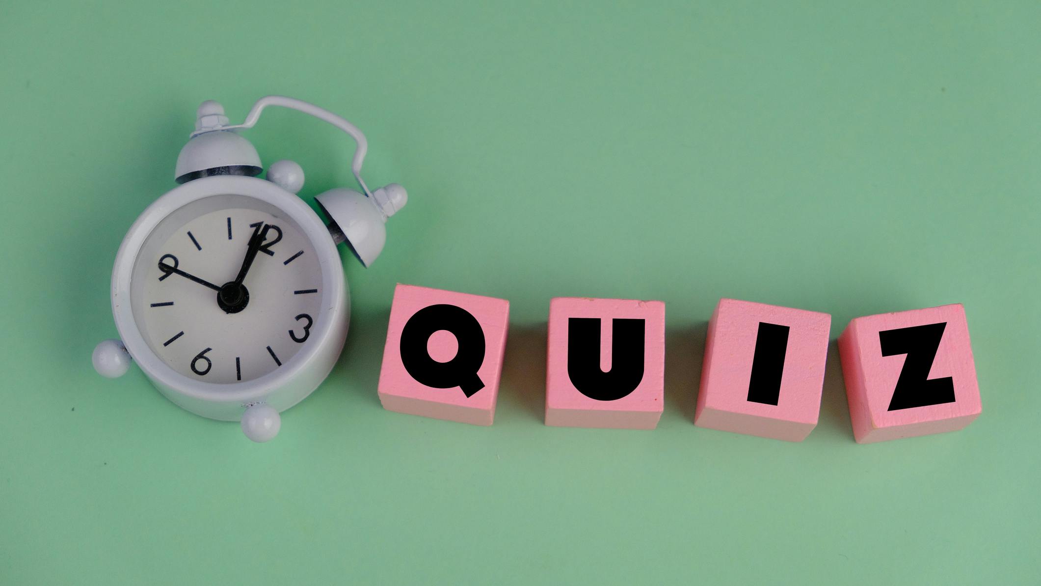 Pink blocks that spell 'quiz' against a light green background next to a white alarm clock.