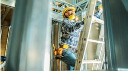 A construction worker wearing a yellow hard hat and yellow tool belt climbs up a ladder. A construction worker wearing a yellow hard hat and yellow tool belt climbs up a ladder.