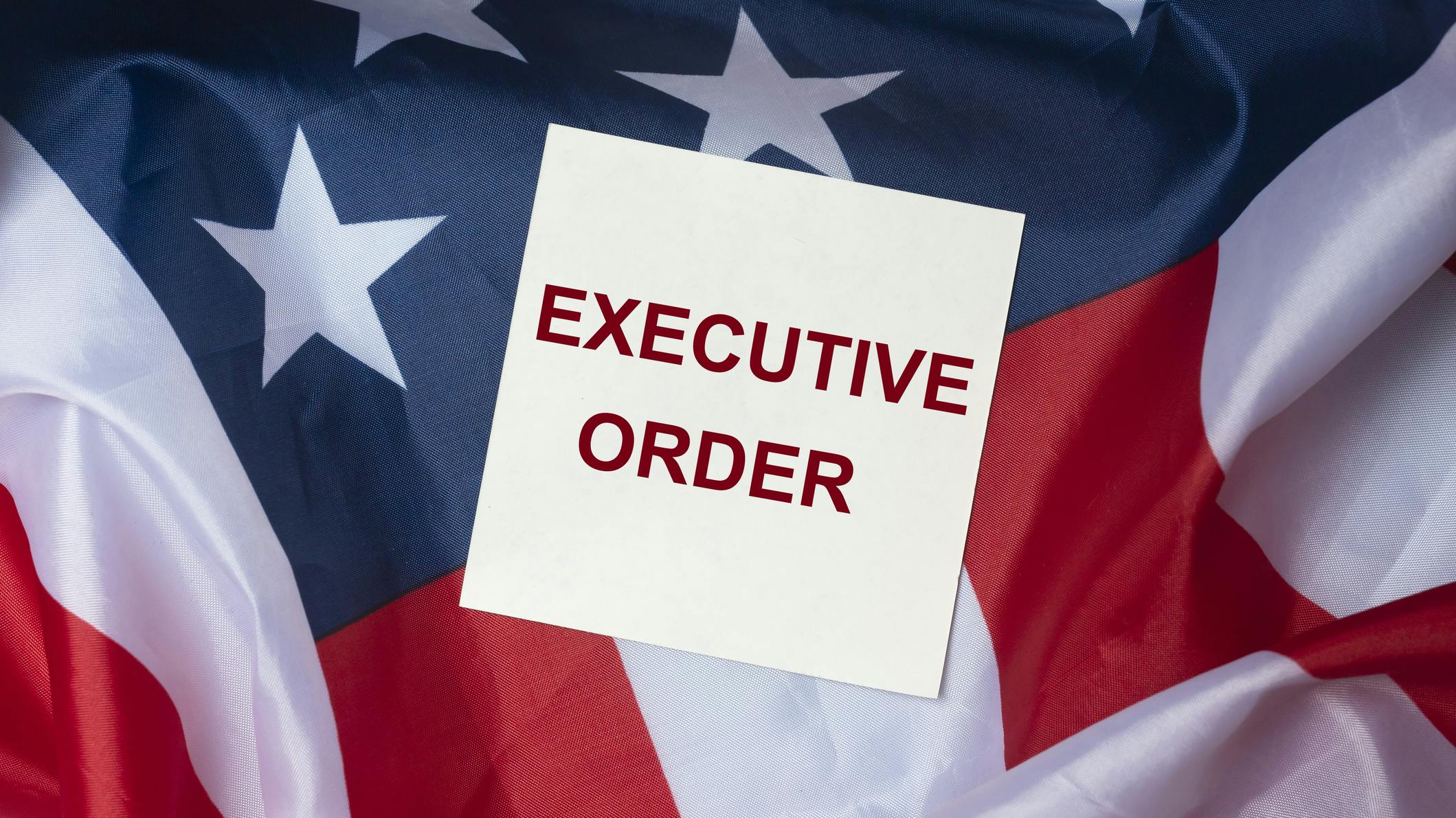 A white box that says 'EXECUTIVE ORDER' in red all caps lays across an american flag background