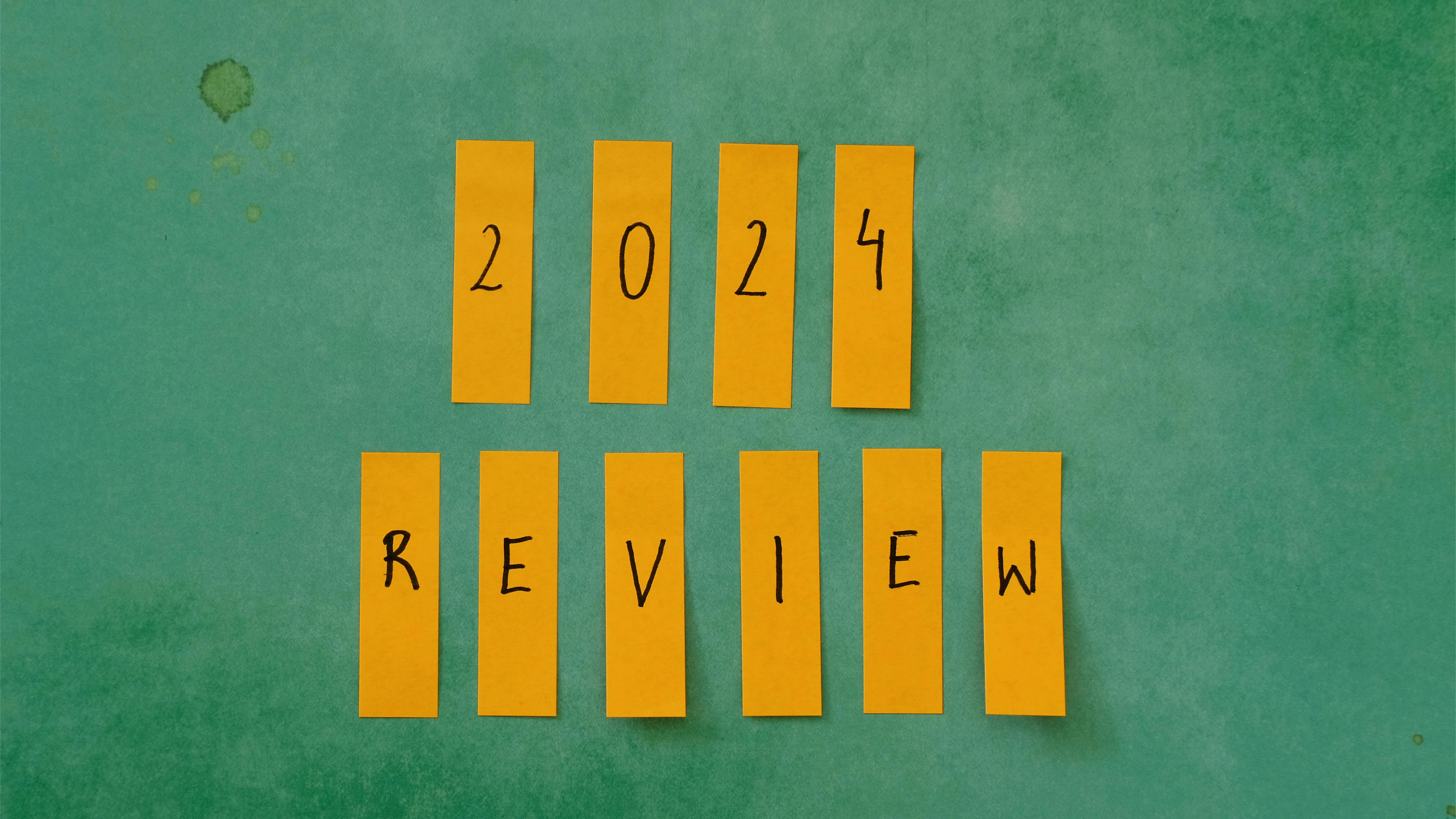 A green chalkboard that says '2024 Review.' Each letter/number is on its own yellow sticky note.