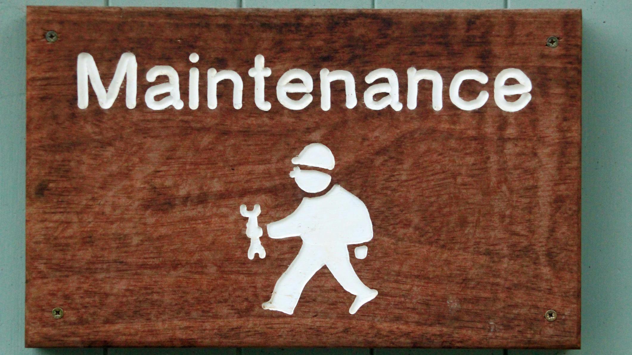 A wooden sign with white writing says 'Maintenance.' Below is a graphic of a construction worker wearing a hard hat and holding a wrench.