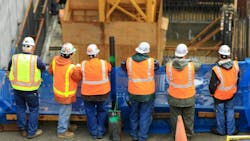 Six construction workers stand in a row with their backs facing the camera. They look onto the job site. Six construction workers stand in a row with their backs facing the camera. They look onto the job site.