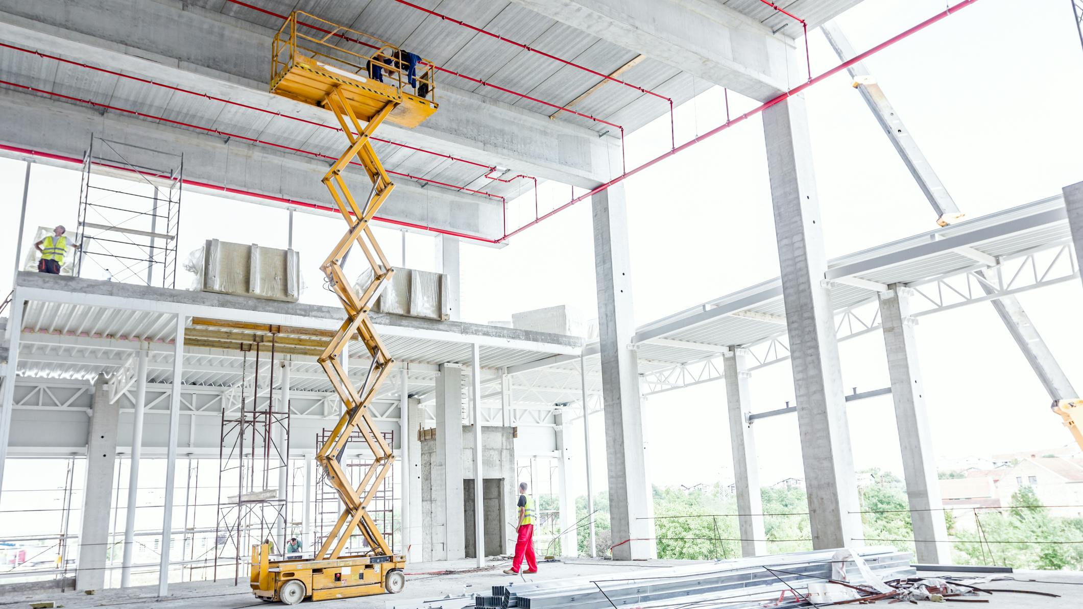 A yellow scissor lift stands in a construction site.