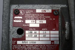 Photo 2. This nameplate on a snap switch enclosure identifies the specific hazardous (classified) locations the enclosure can be installed. The switch handle was removed to obtain this image. This enclosure can be installed in Class I areas, where Groups C or D are present (such as ethylene or propane). It is also identified for installation in Class II areas where Group E or G materials are present (such as certain metal dust or coal dust). Note the “Caution” at the bottom of the nameplate requiring removal of the electrical energy before opening the enclosure to prevent explosions. Photo 2. This nameplate on a snap switch enclosure identifies the specific hazardous (classified) locations the enclosure can be installed. The switch handle was removed to obtain this image. This enclosure can be installed in Class I areas, where Groups C or D are present (such as ethylene or propane). It is also identified for installation in Class II areas where Group E or G materials are present (such as certain metal dust or coal dust). Note the “Caution” at the bottom of the nameplate requiring removal of the electrical energy before opening the enclosure to prevent explosions.