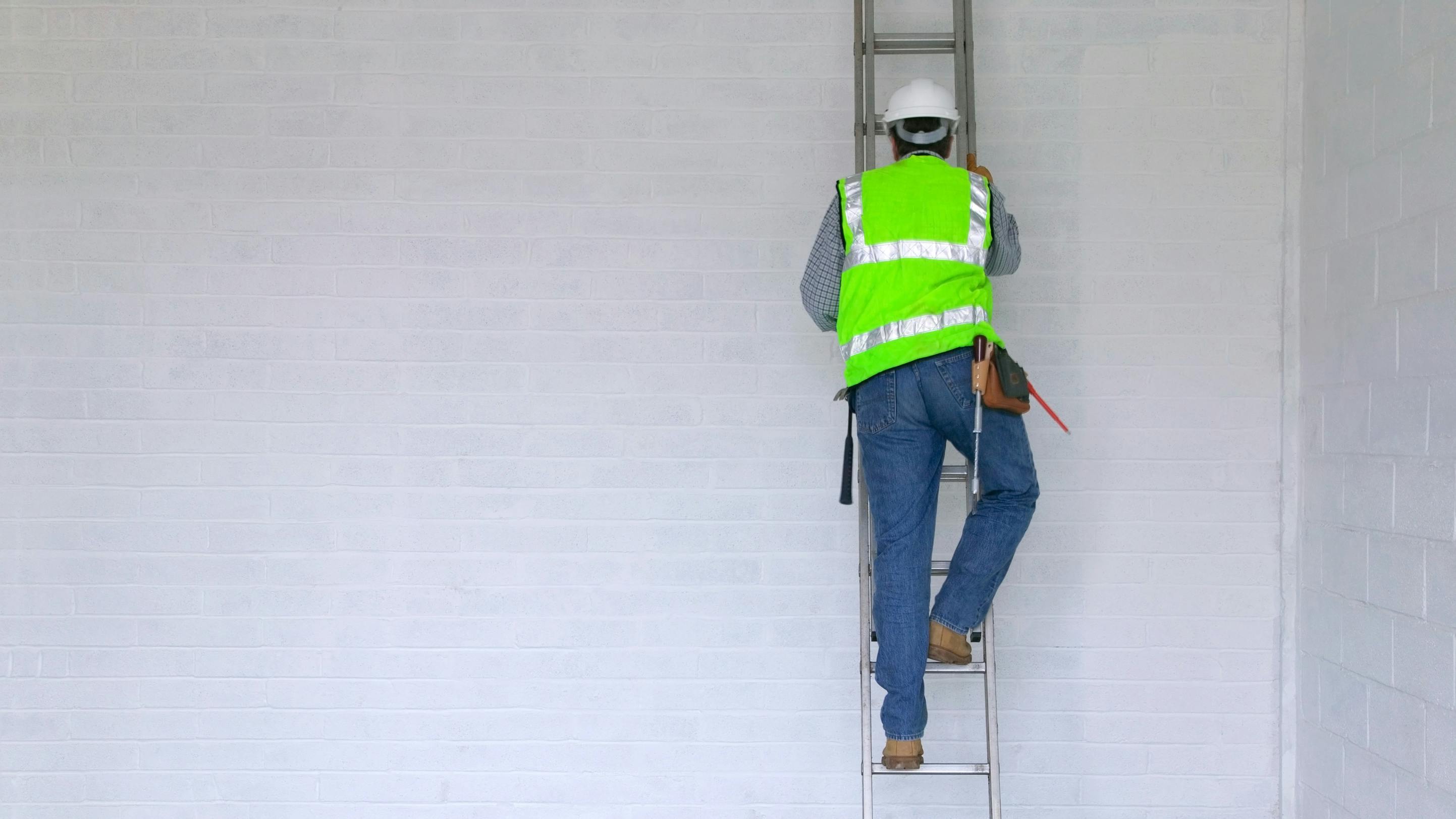 Workman climbing a ladder. Workman in reflective vest and hard hat climbing a ladder, slight motion blur on the man.