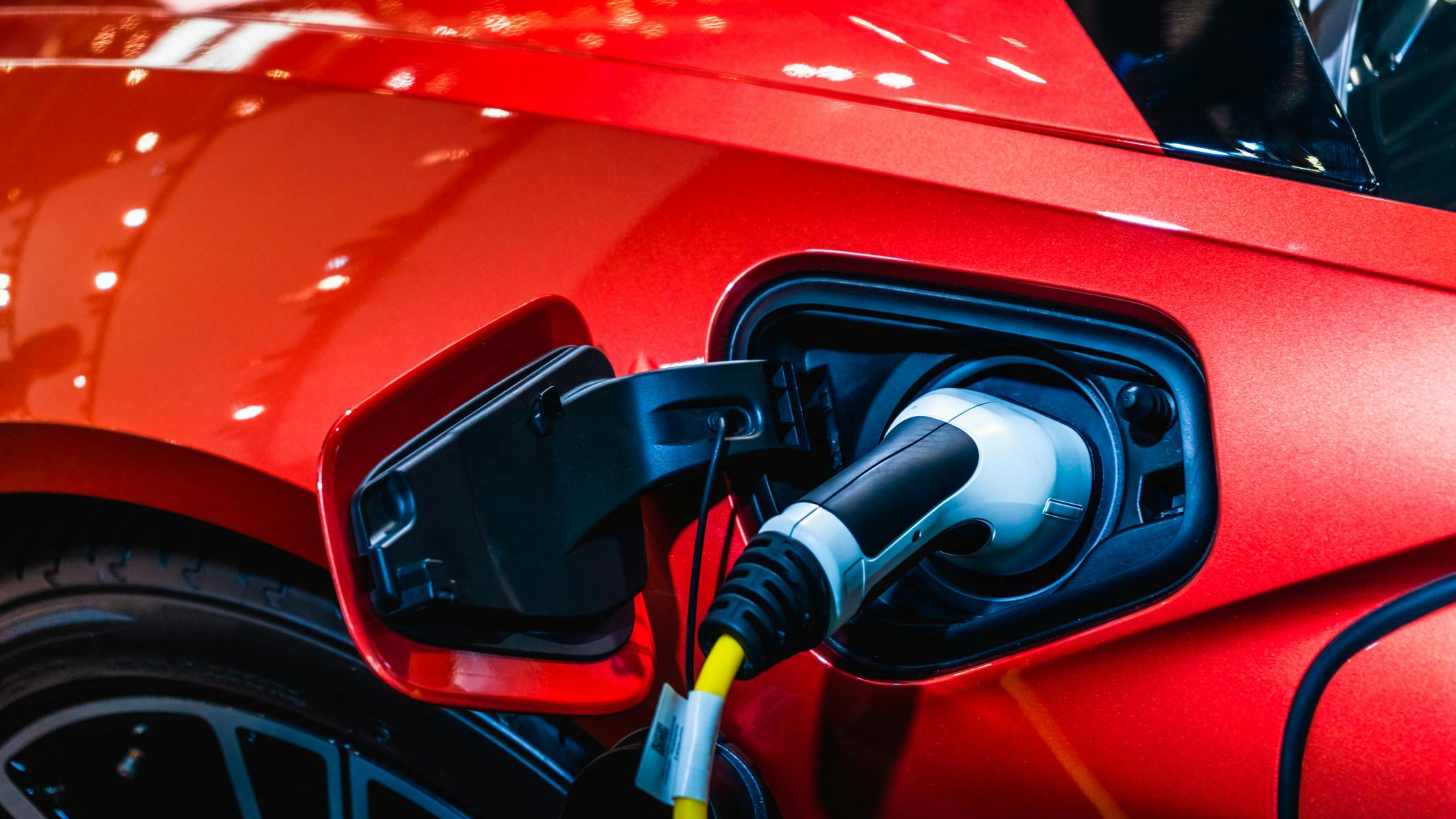 Red EV Car at charging station with the power cable supply plugged in. Power supply connect to electric vehicle for charging the