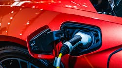 Red EV Car at charging station with the power cable supply plugged in. Power supply connect to electric vehicle for charging the Red EV Car at charging station with the power cable supply plugged in. Power supply connect to electric vehicle for charging the