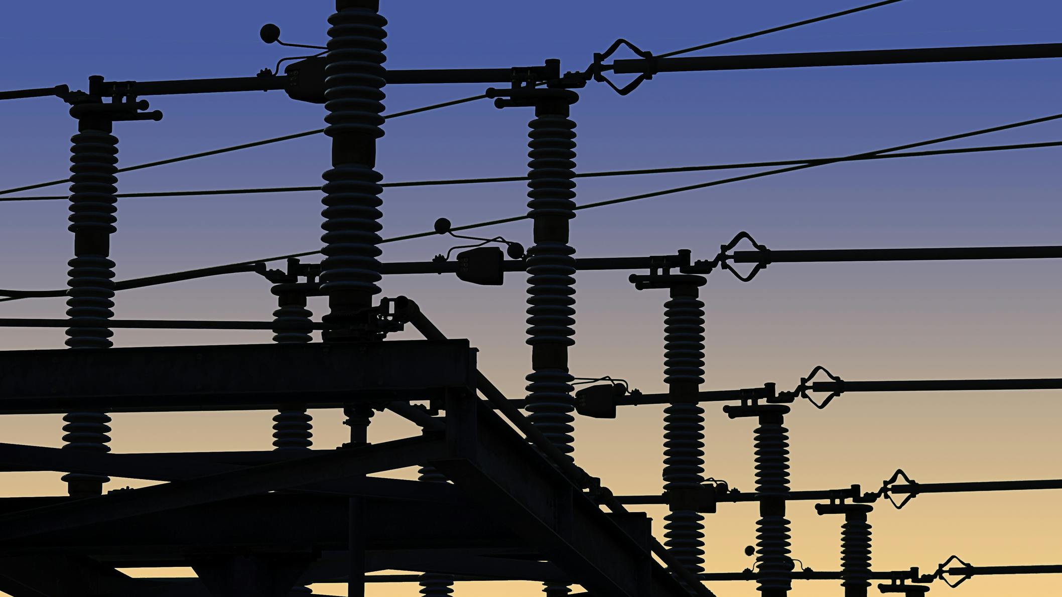 Electrical power grid in silhouette against blue and yellow sky