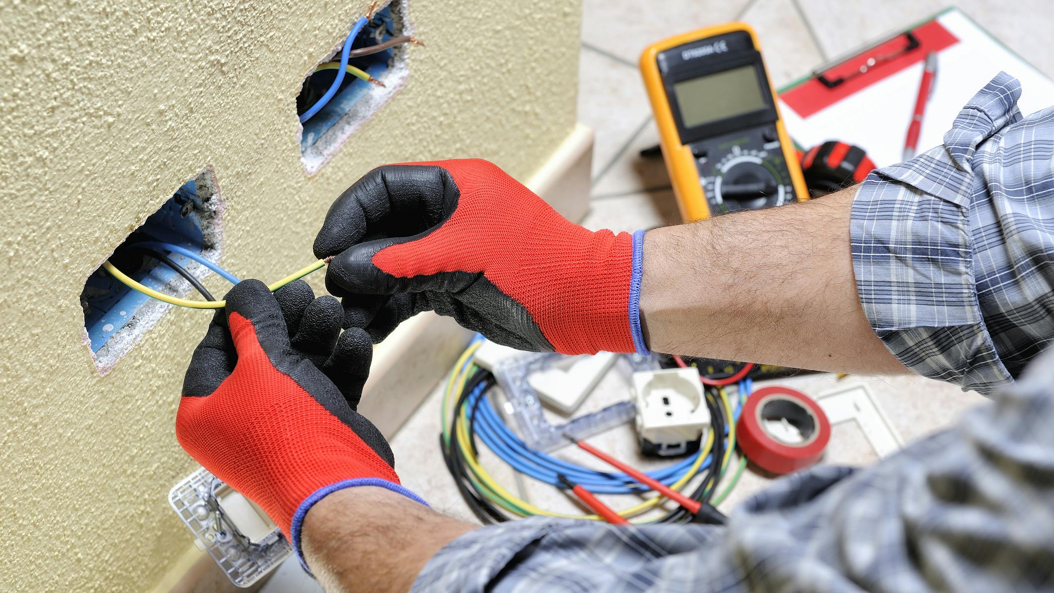 Electrician technician at work with safety equipment on a residential electrical system. Electrician technician at work prepares the cable with hands protected by gloves in a residential electrical installation