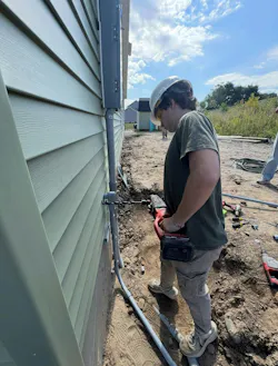 David Hemsworth, an 11th-grade student in the Electrical Construction and Maintenance program at Ulster County Board of Cooperative Educational Services (BOCES), drills through the exterior wall to install a ¾-inch PVC conduit for a #6 stranded copper grounding electrode conductor at an Ulster County Habitat for Humanity home.
