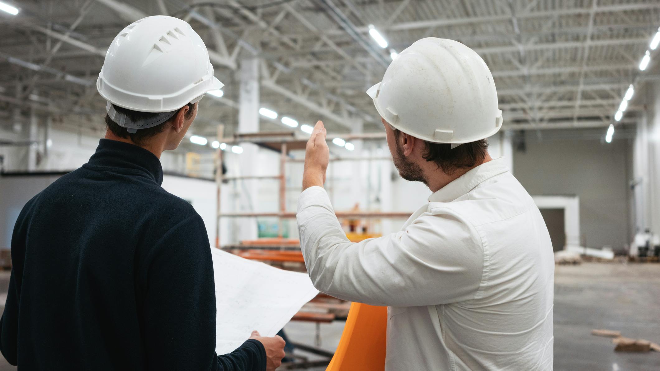 Architect and builder look on blueprint building under construction. Engineer and worker wearing safety hard hat have meeting on construction site