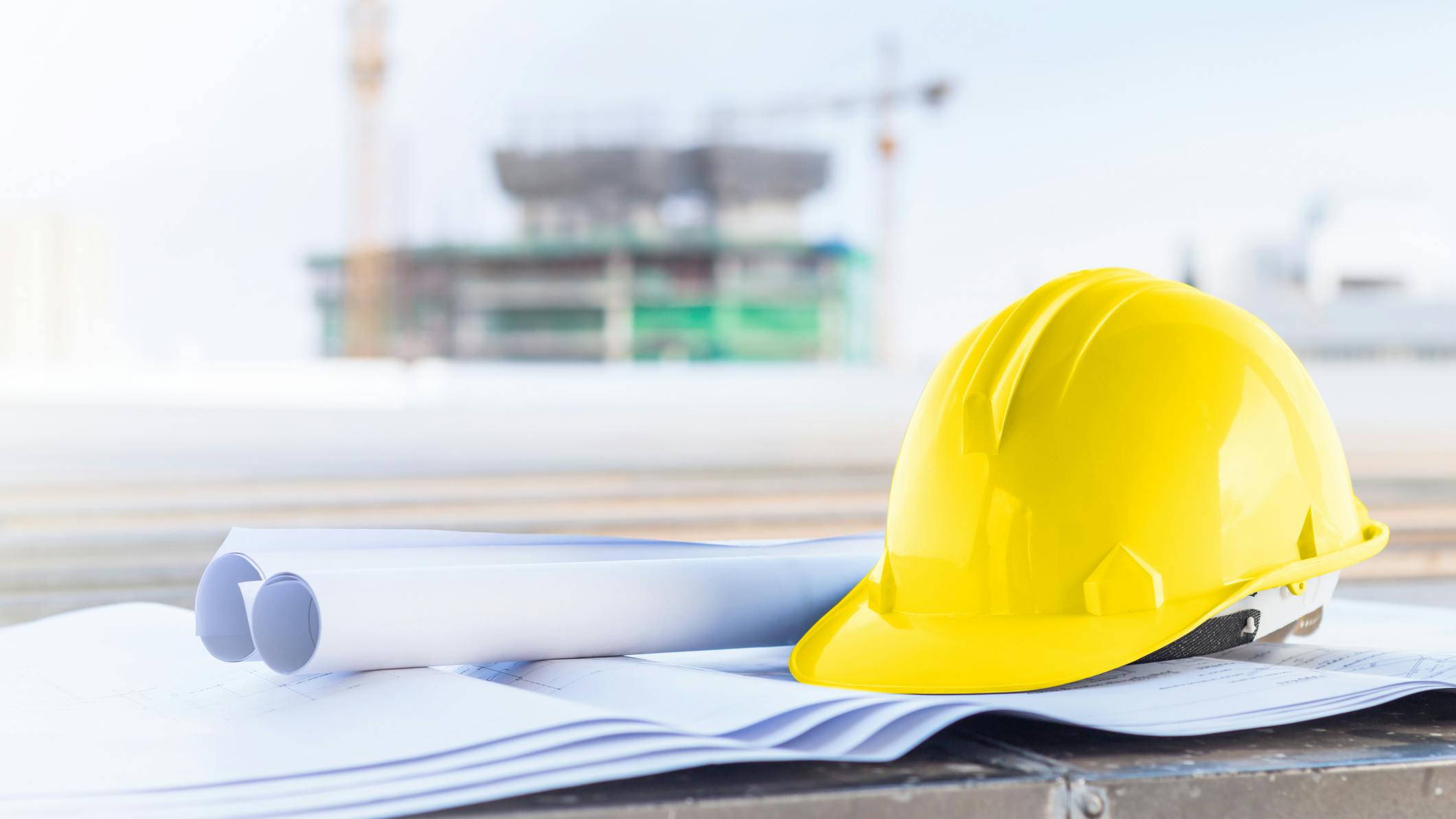 The yellow safety helmet and the blueprint at construction site with crane background.