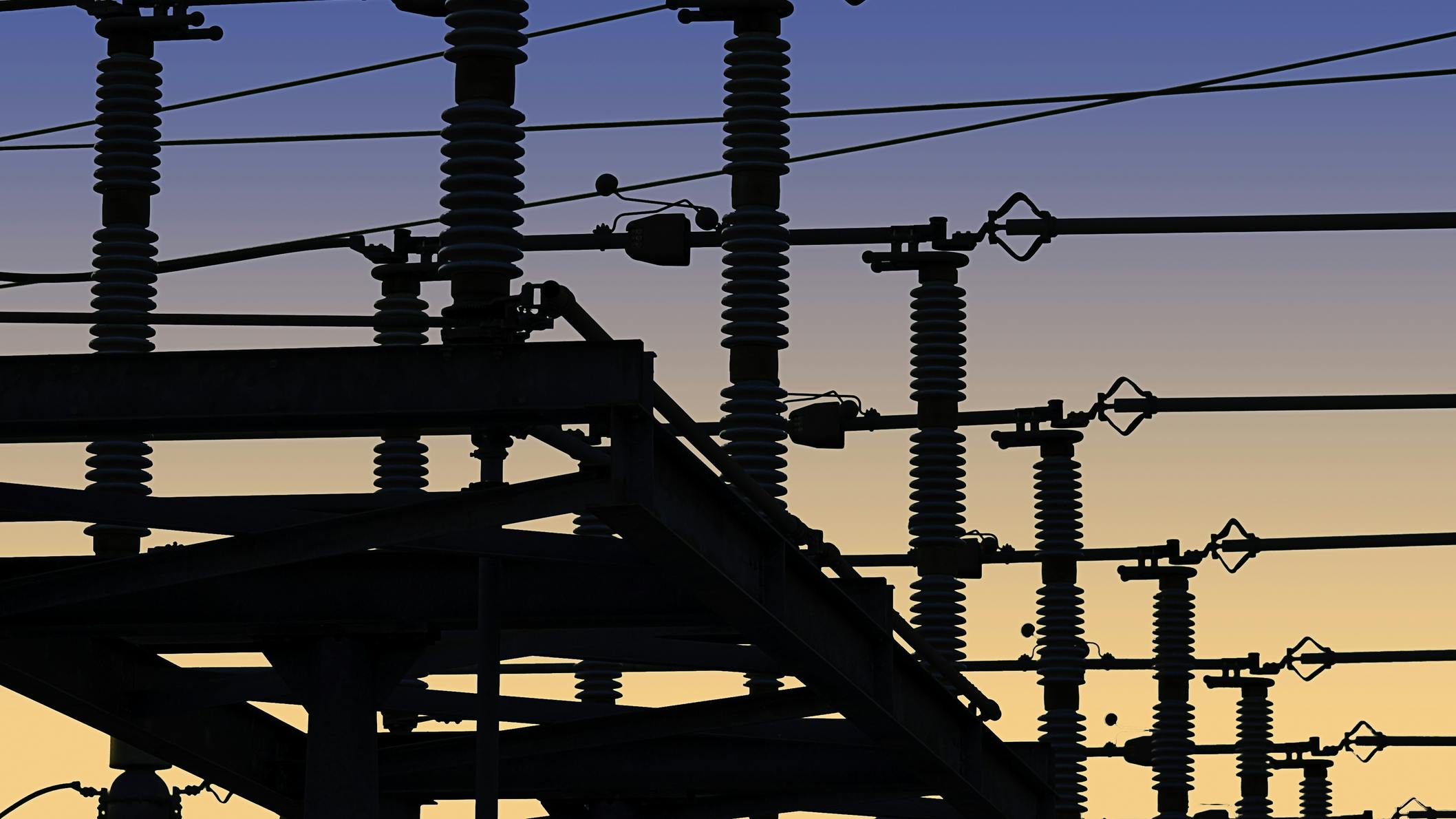 Electrical power grid in silhouette against blue and yellow sky